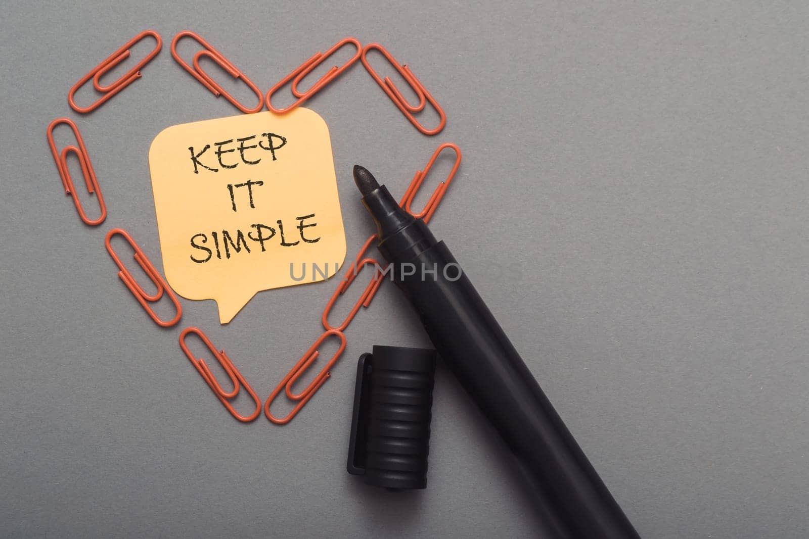 Keep it simple is written on a yellow sticky note on a gray desk.