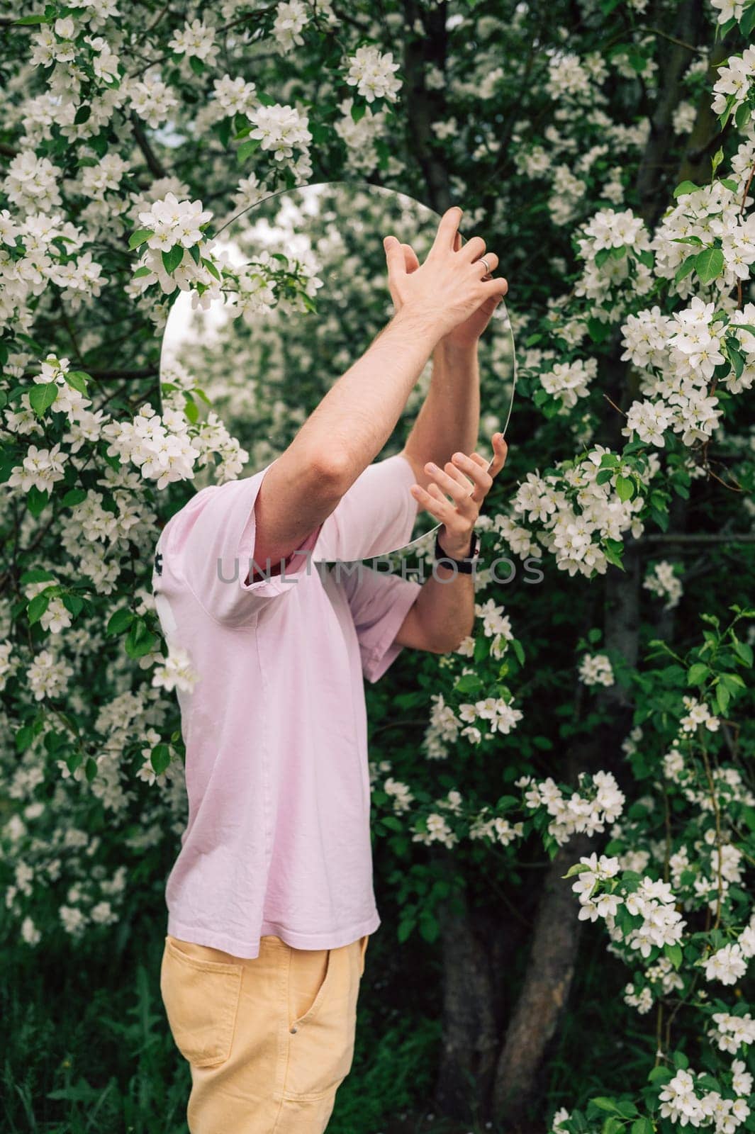 Creative male portrait with mirror in a blooming apples spring garden