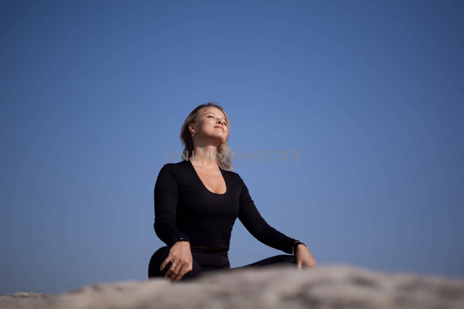 A woman is sitting on a rock and looking up at the sky. She is in a peaceful and contemplative mood