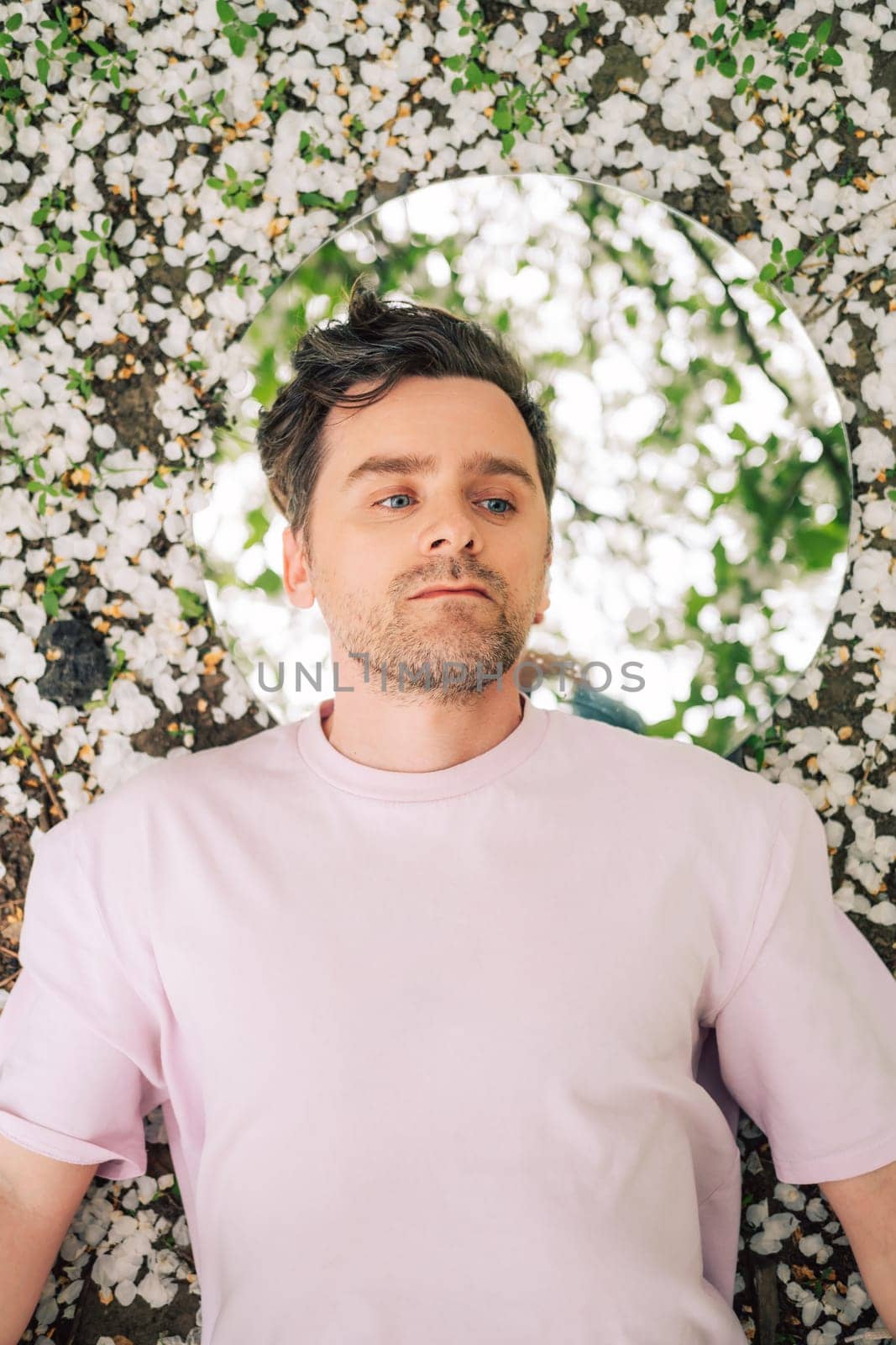 Creative male portrait with mirror lying in the ground in a blooming apples spring garden