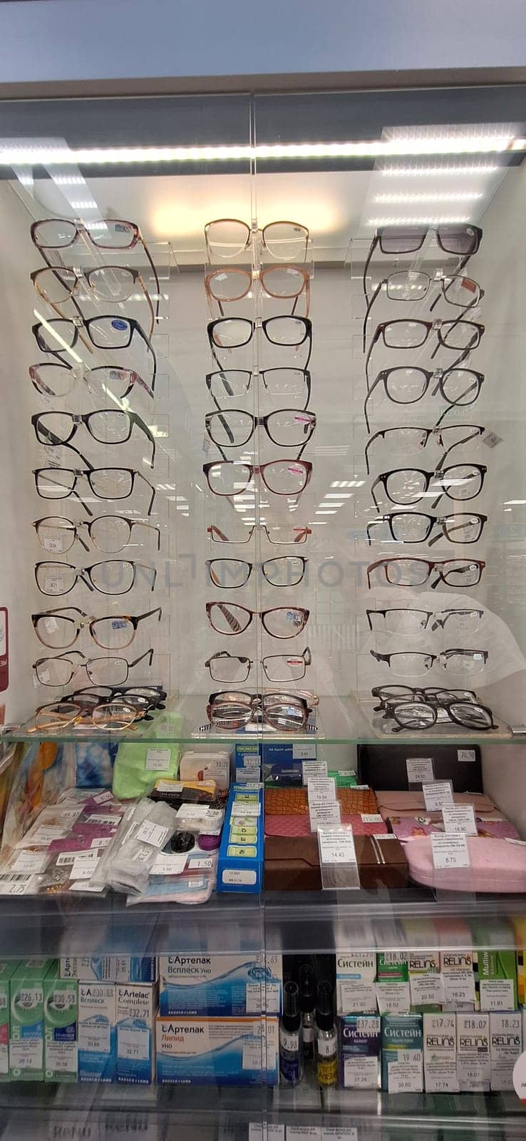 Bobruisk, Belarus - May 1, 2024: A variety of eyeglasses are neatly showcased in a well-lit pharmacy, with medicinal products displayed below.