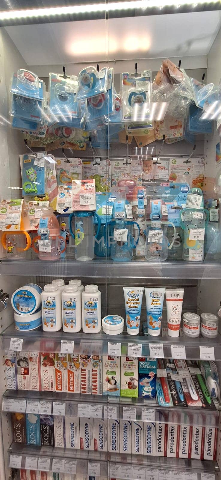 Bobruisk, Belarus - May 1, 2024: A well-organized pharmacy display case showcasing baby pacifiers, feeding bottles, baby powder, baby cream, and toothpaste on a bright day.