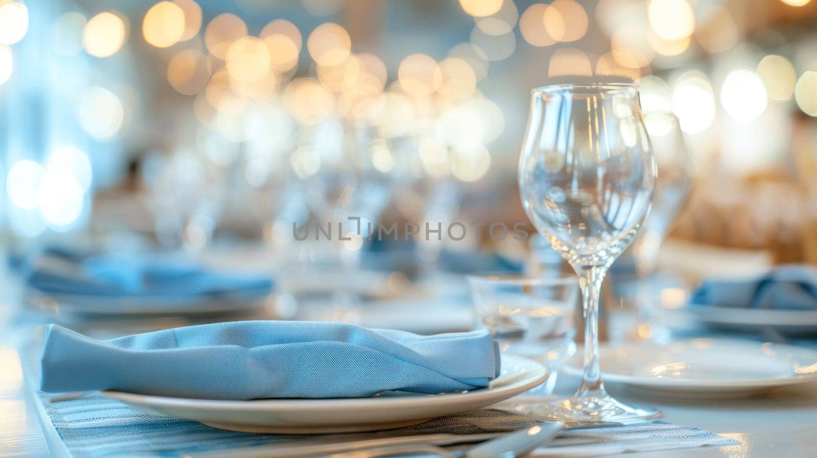 Elegant table setting with blue napkins and wine glasses on white table with bokeh lights in background