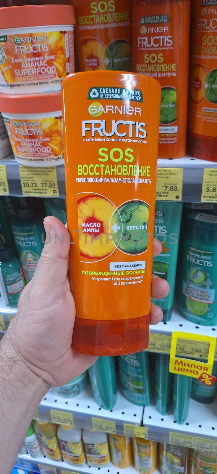 Bobruisk, Belarus - May 1, 2024: A person holds a bottle of Garnier Fructis SOS Restoration Balm in the shampoo aisle of a grocery store, showcasing the product.