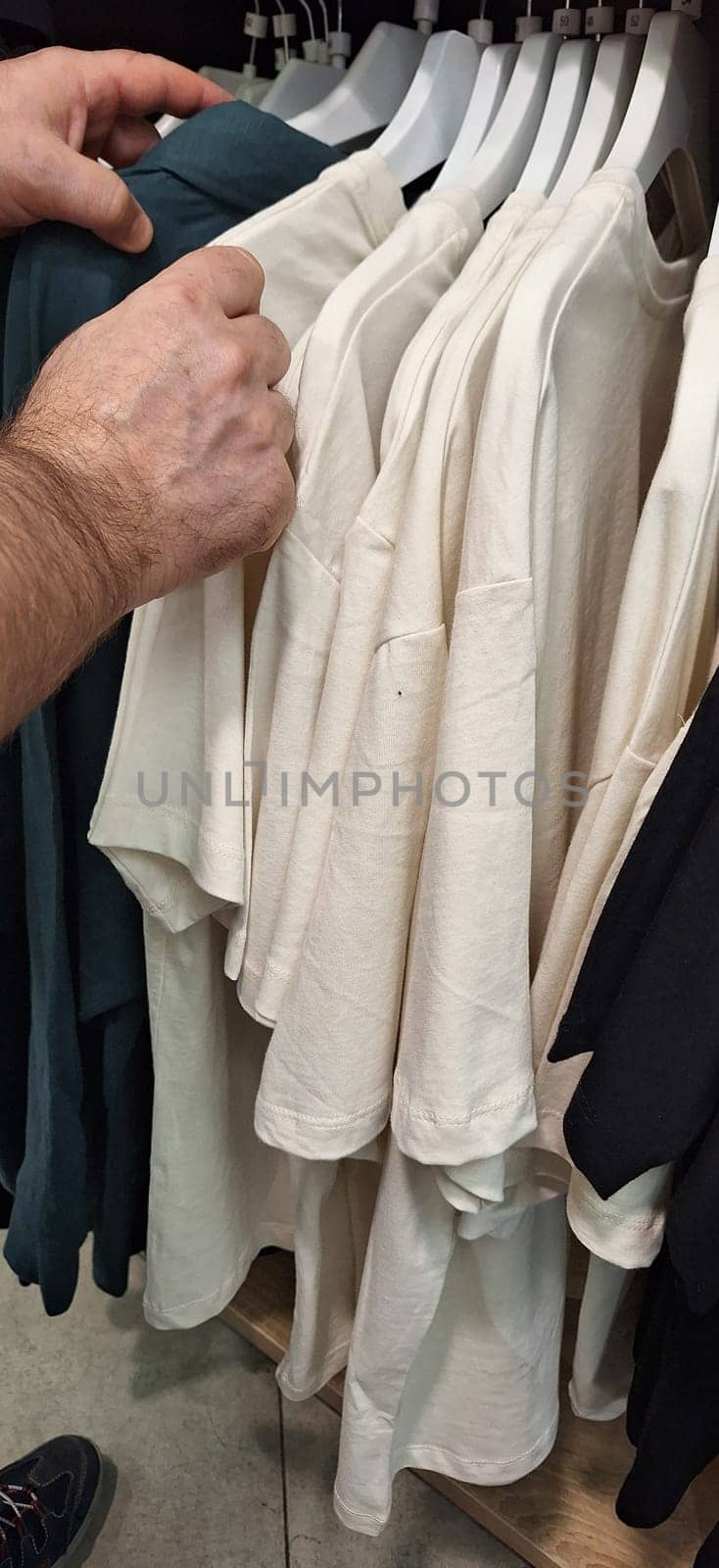 A person standing in front of a rack of shirts, holding one up for inspection.