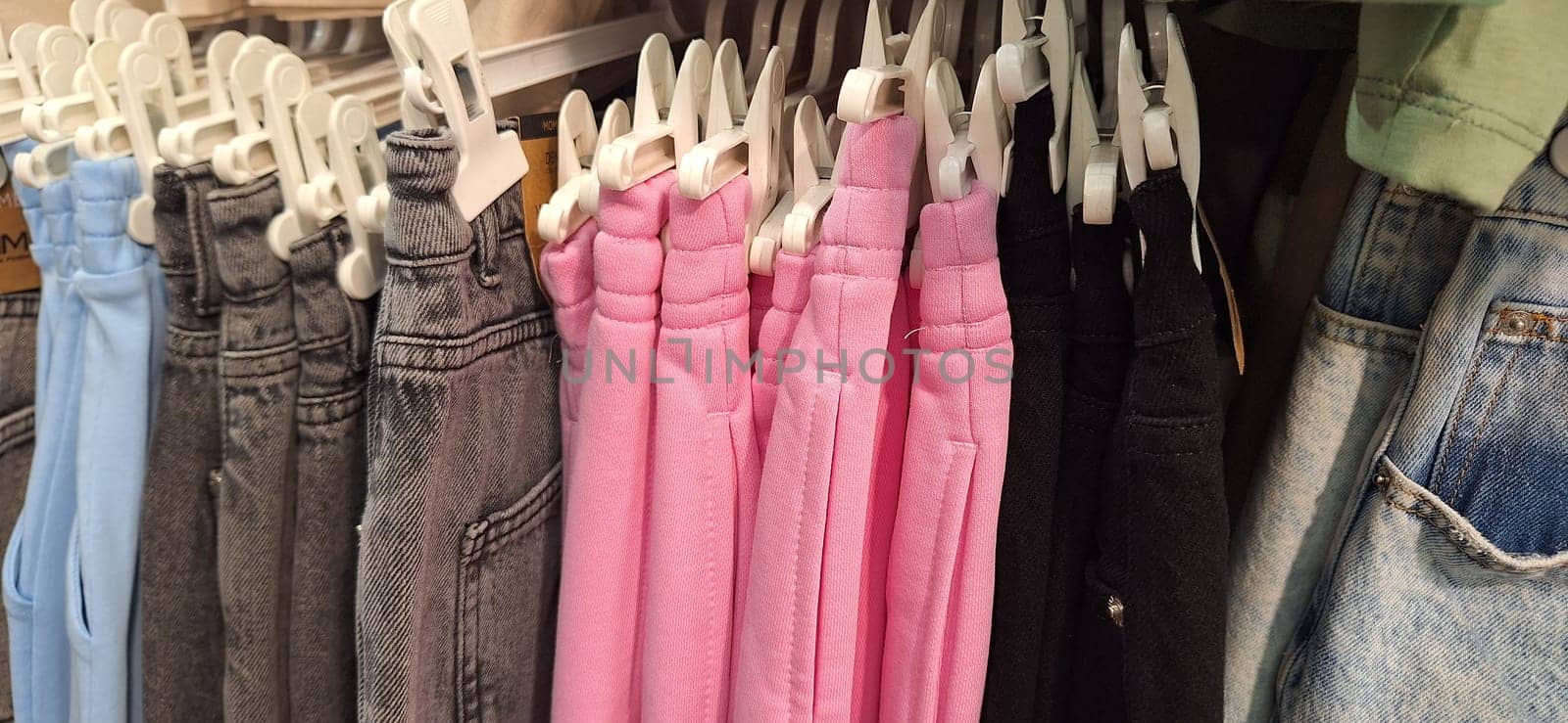 Different colored pants neatly hung on hooks in a rack. Variety of styles and sizes displayed in an organized manner.