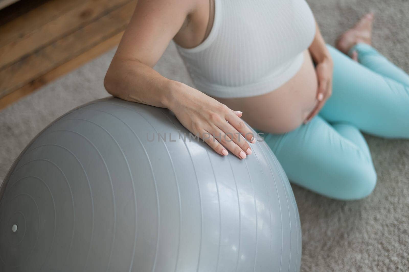 Pregnant woman resting after workout sitting on the floor near the fitness ball