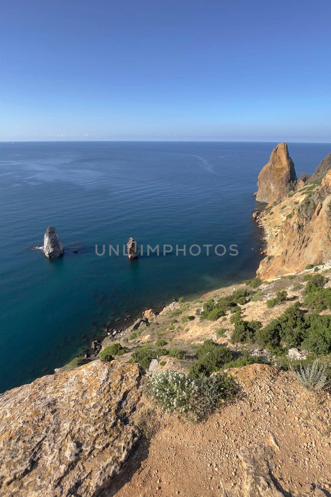 A rocky cliff overlooks the ocean with a blue sky in the background by Matiunina