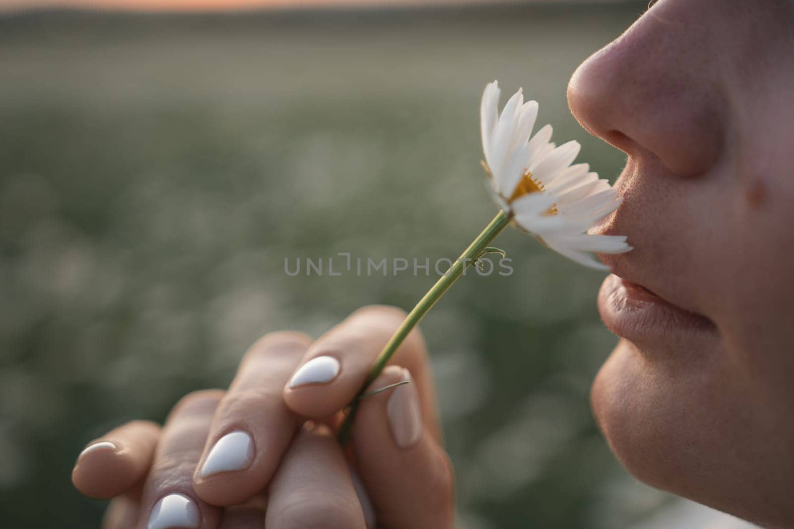 A woman is smelling a flower. The flower is white and has a green stem. The woman is looking at the flower with a smile on her face