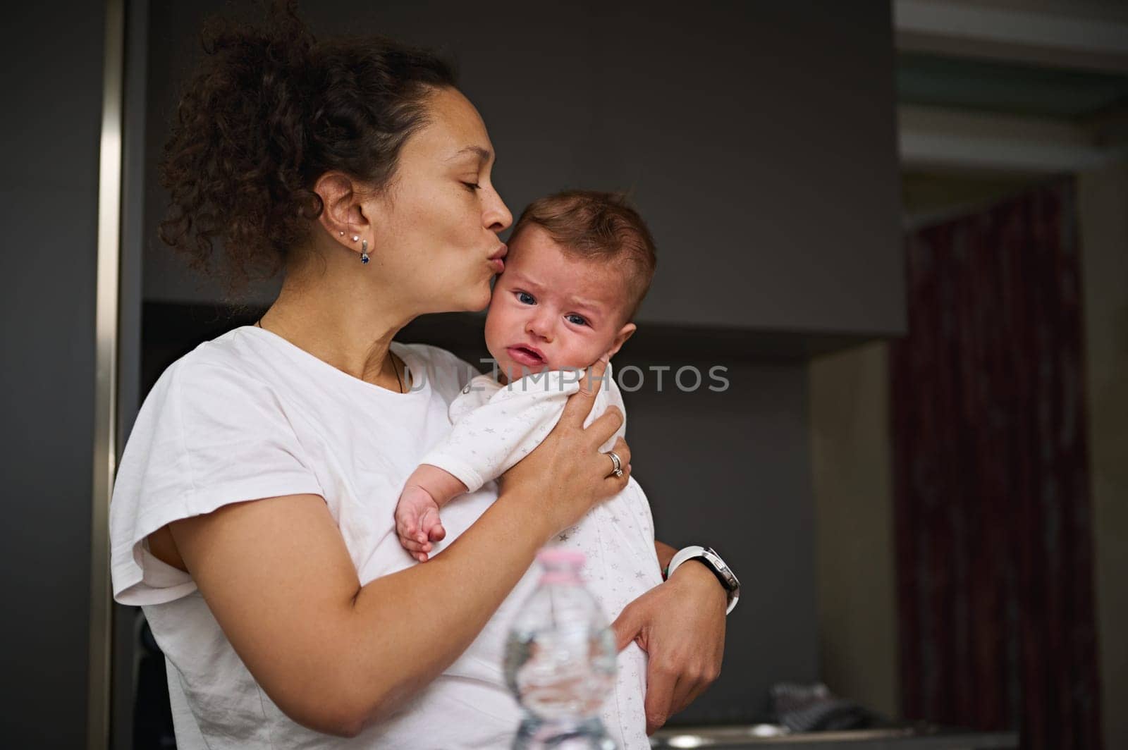 Affectionate young mother kissing temple of her child's head, measuring temperature of her crying baby boy. Childcare. Health check. Babyhood. Maternity. Infancy. Health care and Pediatrics medicine by artgf