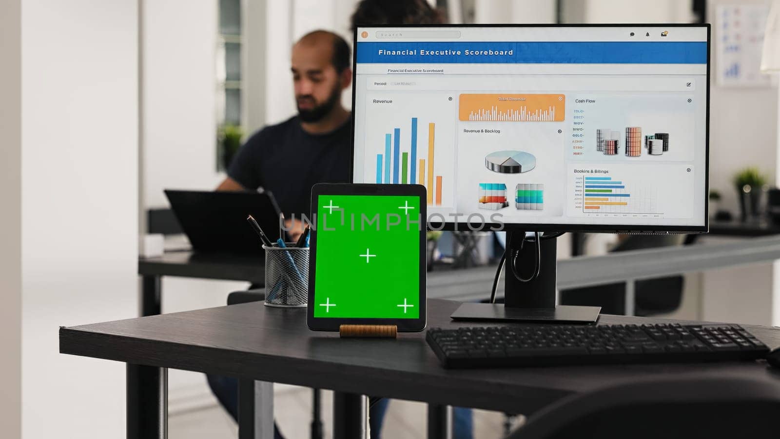 Empty desk with greenscreen tablet and computer running operational data, coworking space for business tasks. Computer desktop at workstation with blank chromakey mockup software on gadget.