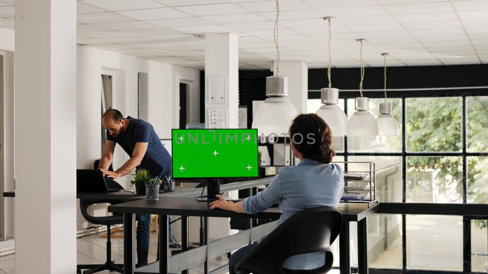 Office worker uses greenscreen on desktop and analyzing isolated software for business operations. Employee looking at monitor showing blank chromakey template at desk. Handheld shot.