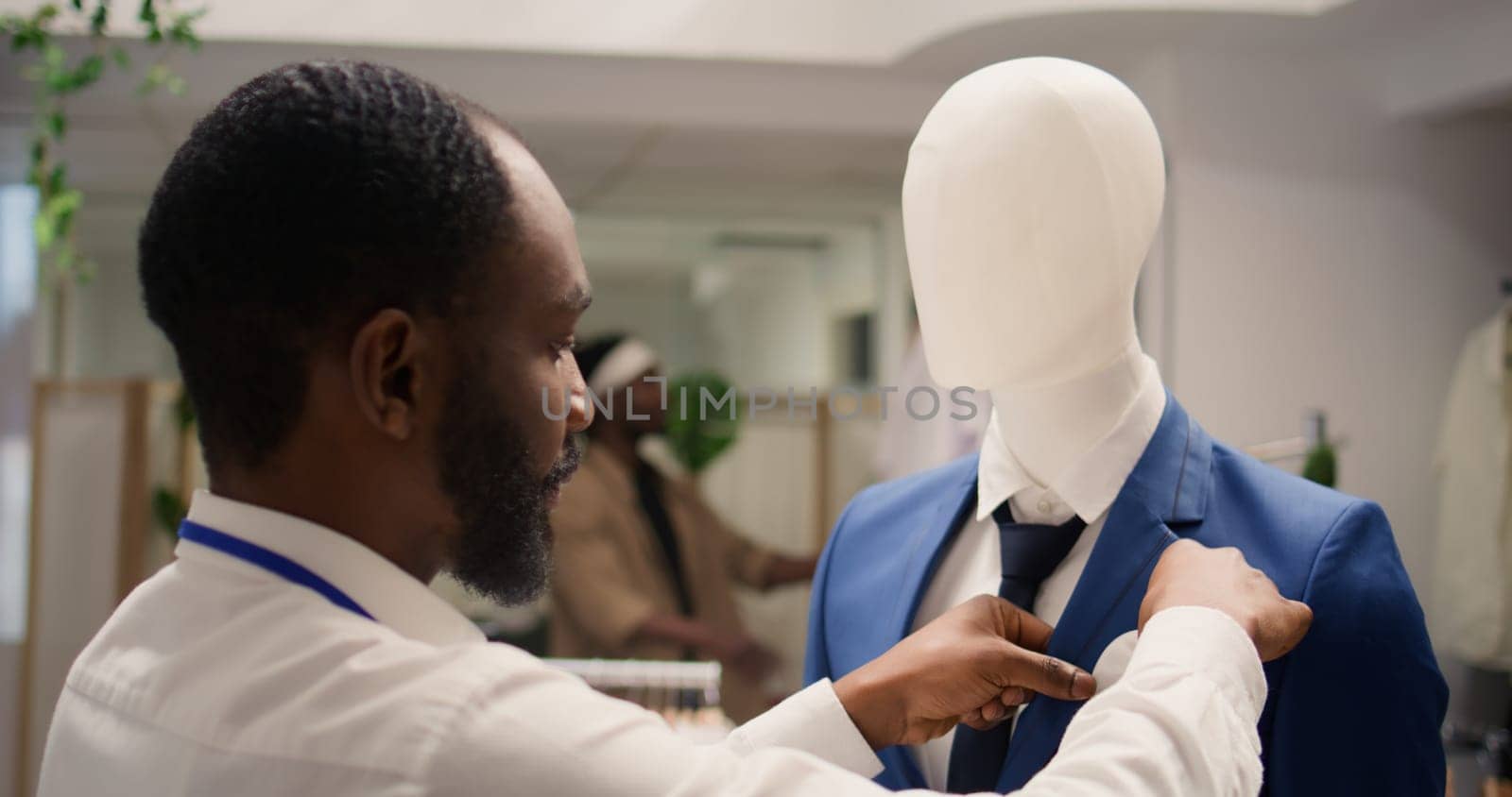 Employee working in clothing store during promotional season, arranging necktie on mannequin blazer. Shopkeeper placing pocket square on older collection garment on sale in fashion boutique