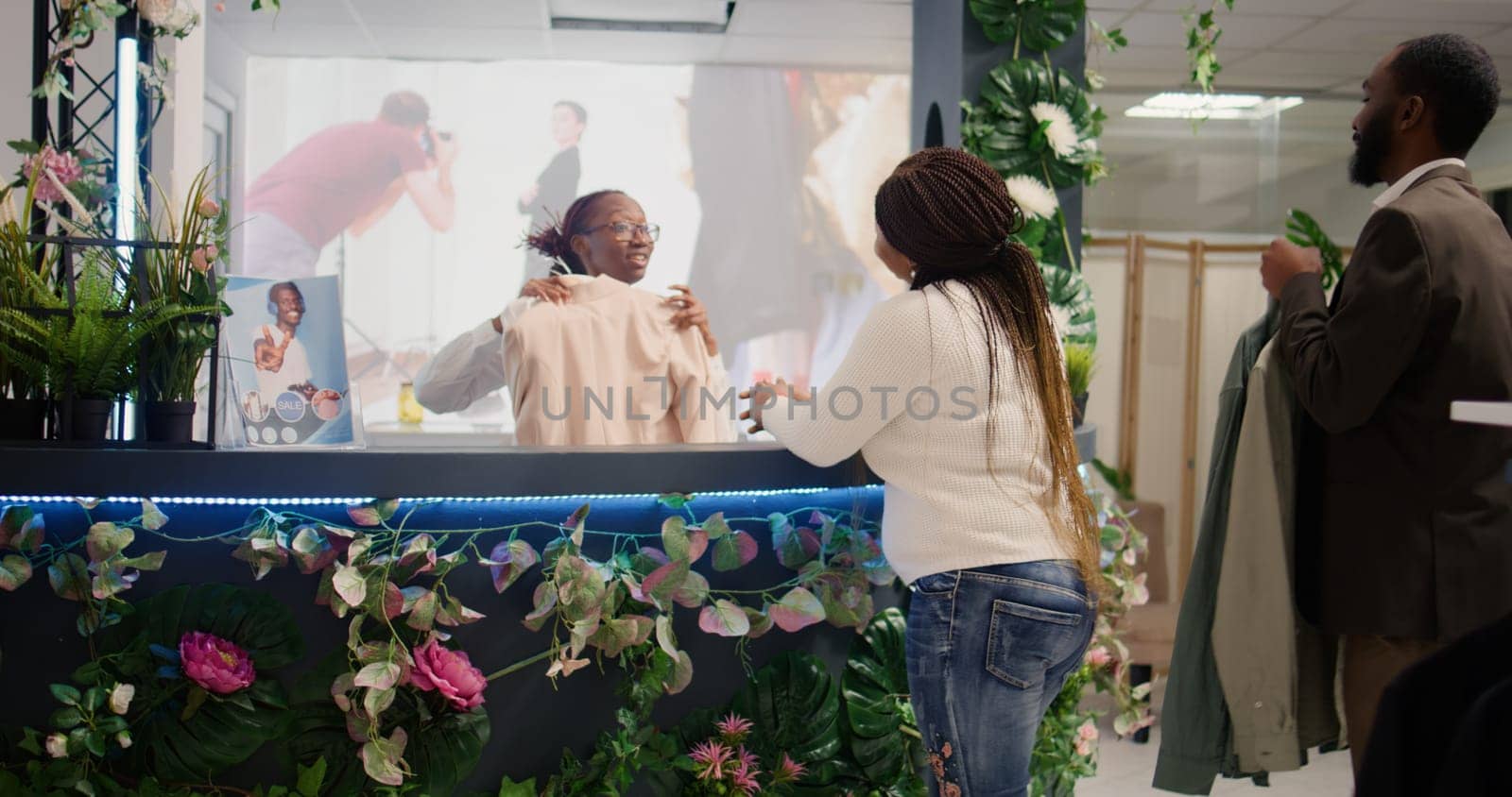 Customers in elegant clothing shop paying for stylish clothes at checkout counter, helped by friendly worker. Shopkeeper assisting shoppers with their purchases in fashion boutique, dolly in shot