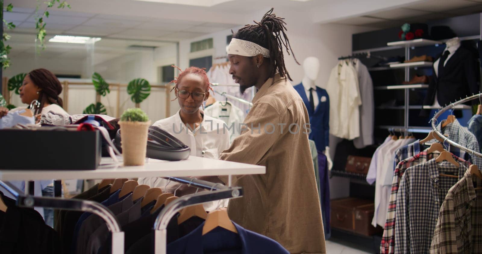 Customer receiving advice from employee in clothing store during promotional season while looking to buy cheap garments to fill his wardrobe. Man helped by worker to find sales in fashion boutique