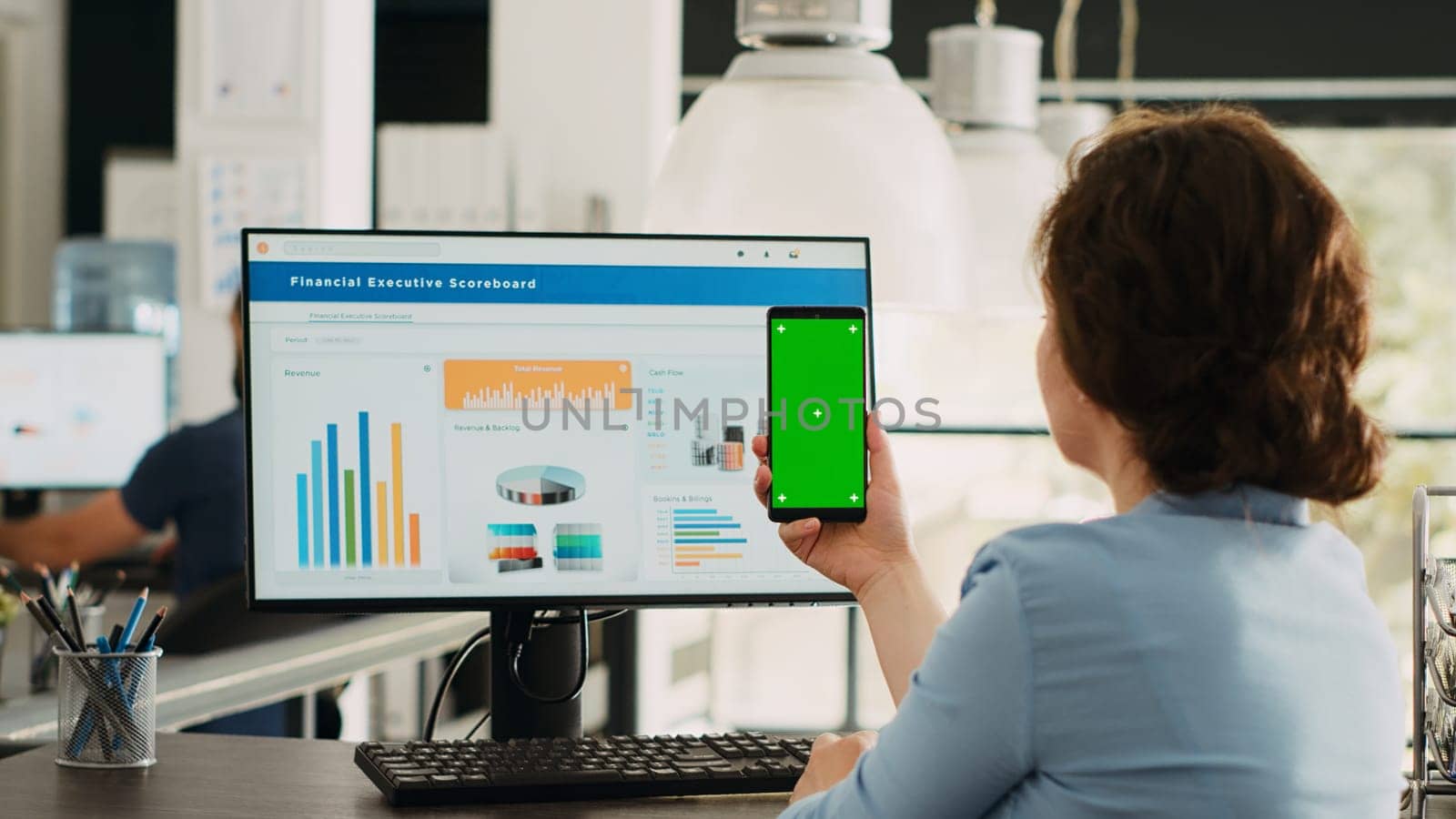 Employee looks at greenscreen on phone, working on business operations at desk. Person holding smartphone device with isolated display showing mockup template, blank layout screen.