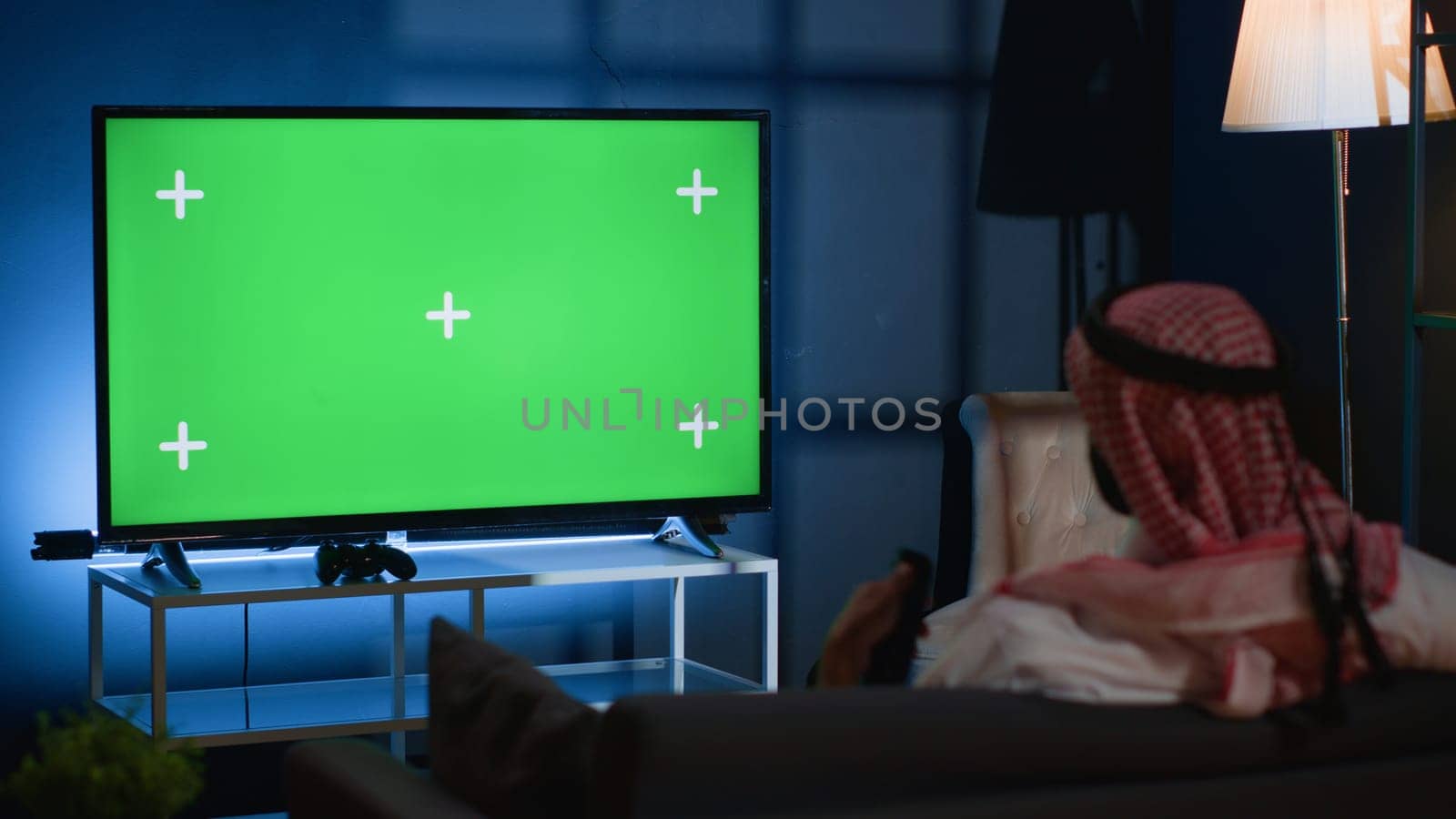 Arab man watching news broadcast on chroma key device while relaxing at home after hard day at work. Muslim person chilling on couch, looking at isolated screen TV channel