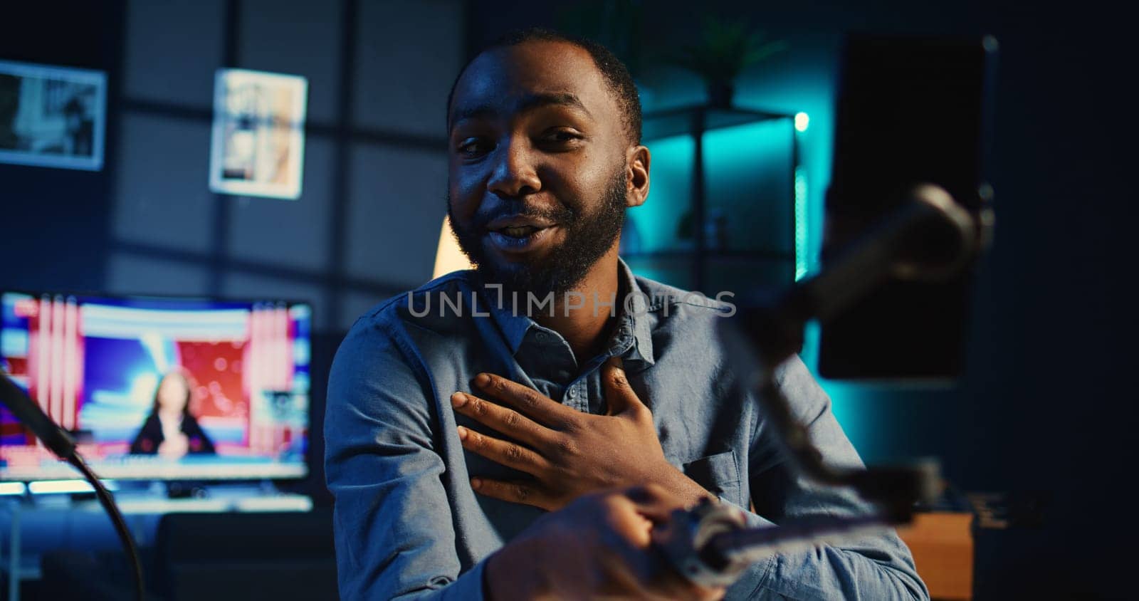 BIPOC content creator using selfie stick smartphone, doing video for fans showing his cozy apartment studio. Media star talking with audience during online stream using mobile phone camera