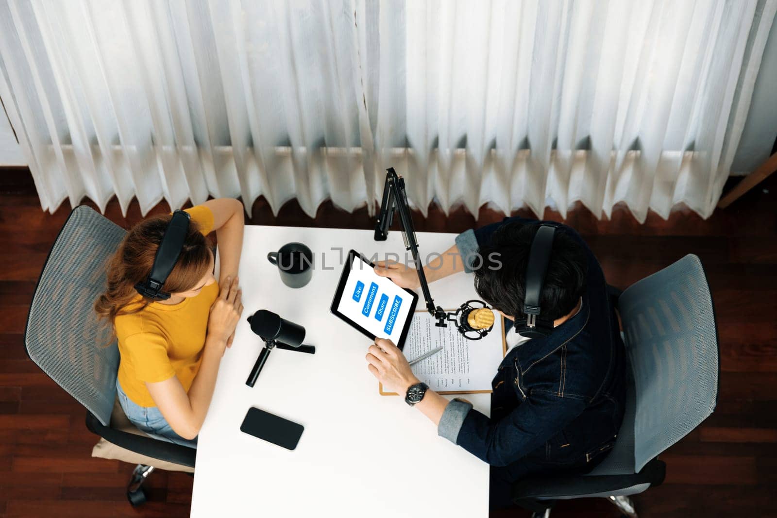 Top view of smiling radio influencer hosts wearing headphone with channel social media online live streaming with talking with tablet screen share to listeners at morning at studio record. Infobahn.