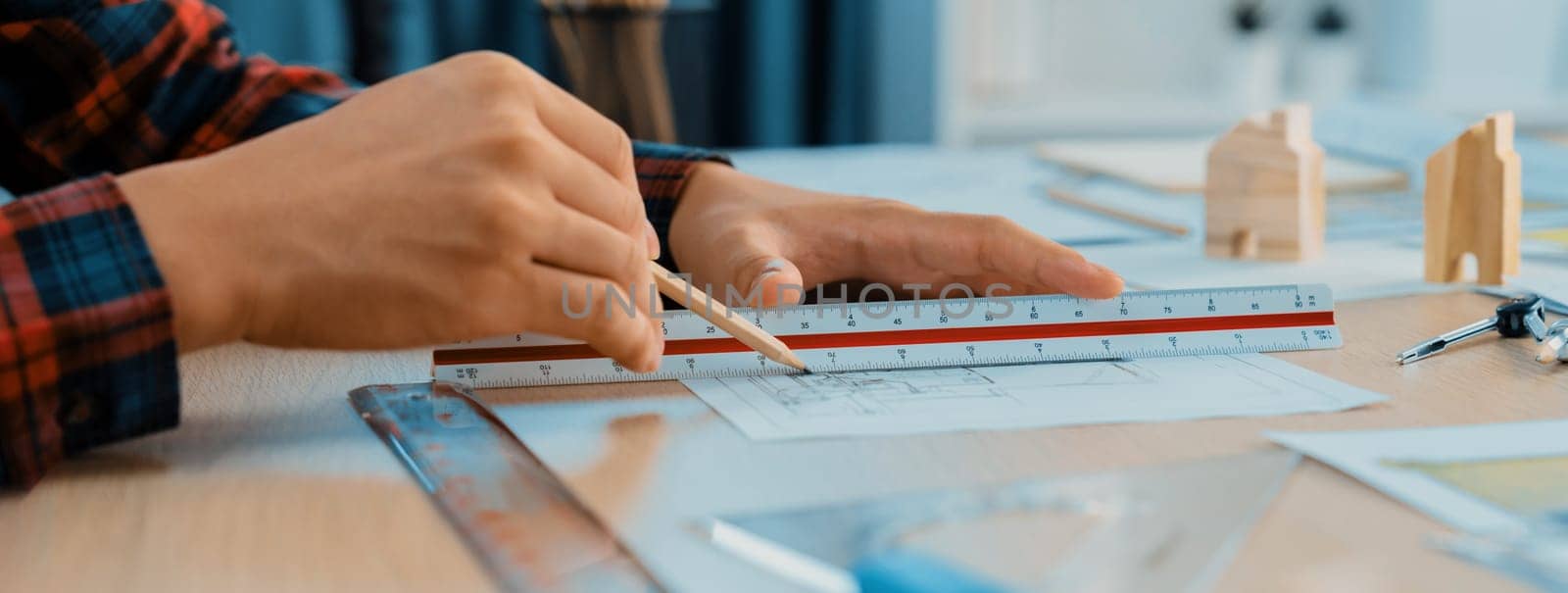 Closeup of architect engineer hand using ruler to mature and draw a blueprint on meeting table with wooden block, pencil and blueprint scatter around at architectural modern office. Delineation.