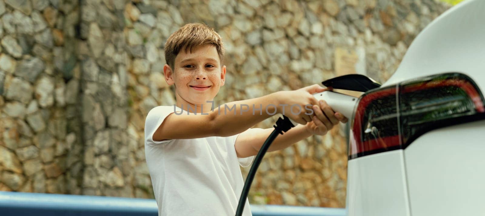 Little boy recharging eco-friendly electric car from EV charging station. EV car road trip travel concept for alternative transportation powered by clean renewable and sustainable energy. Perpetual