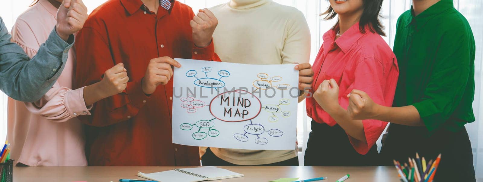 A cropped image of successful businesspeople presents new product marketing strategy using a mind map. Young creative business team brainstorm marketing idea together at modern office. Variegated.