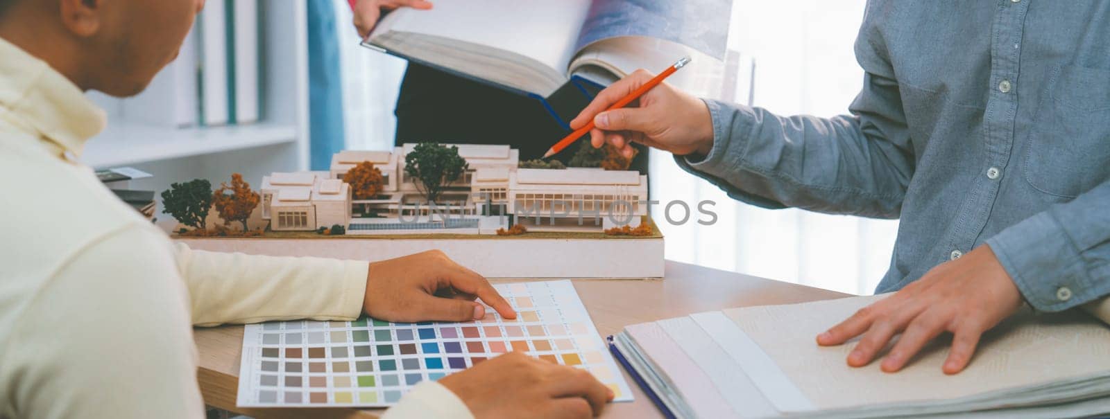 Cropped image of professional interior design team discuss about color and material usage for the project while project manager choose main theme color with house model on meeting table. Variegated.