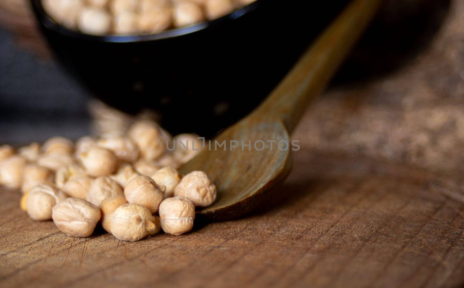 Chickpeas grains falling from a wooden spoon .Dark background.  by VeroDibe