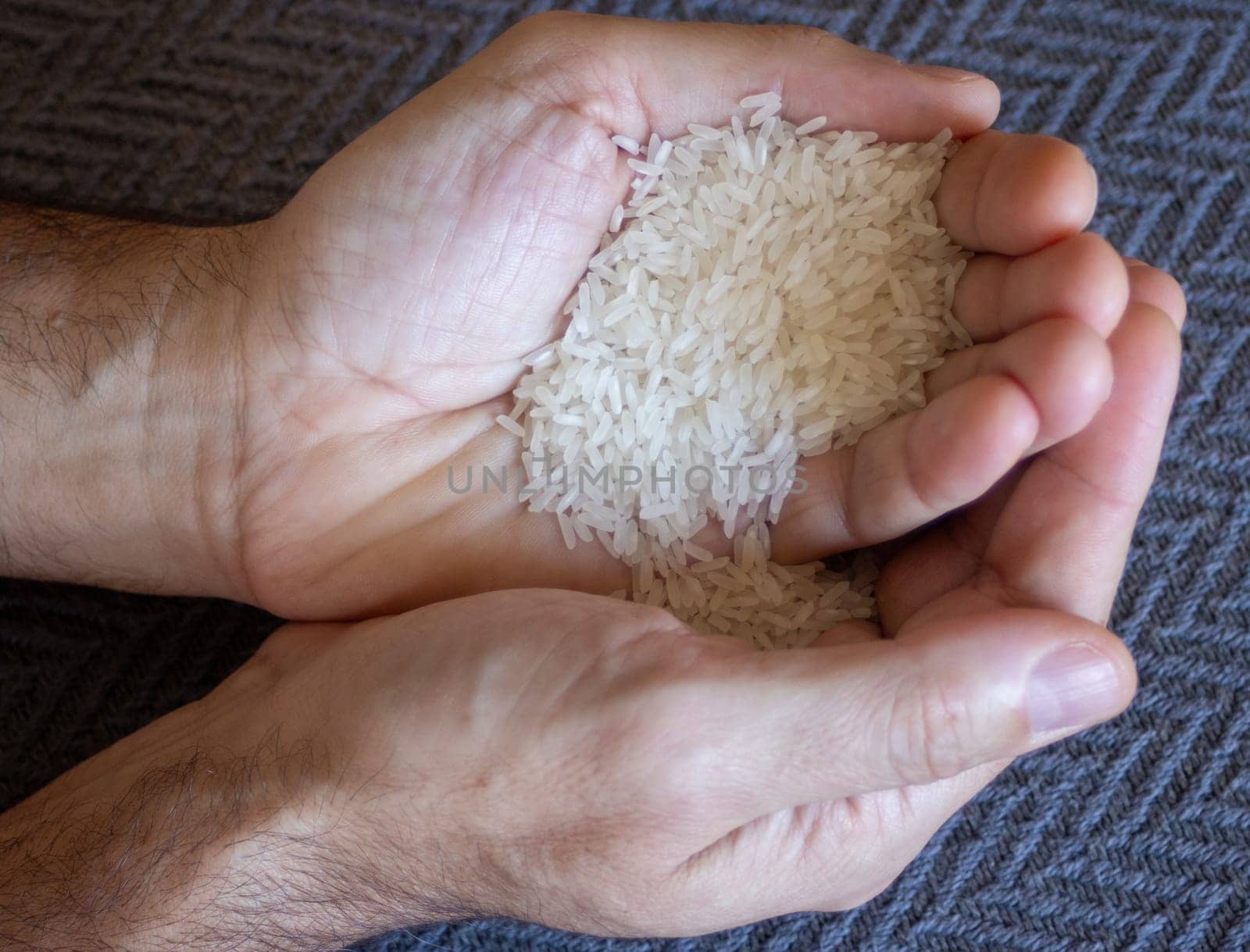 Very close-up photo of rice grains on young man hands. Dark background by VeroDibe