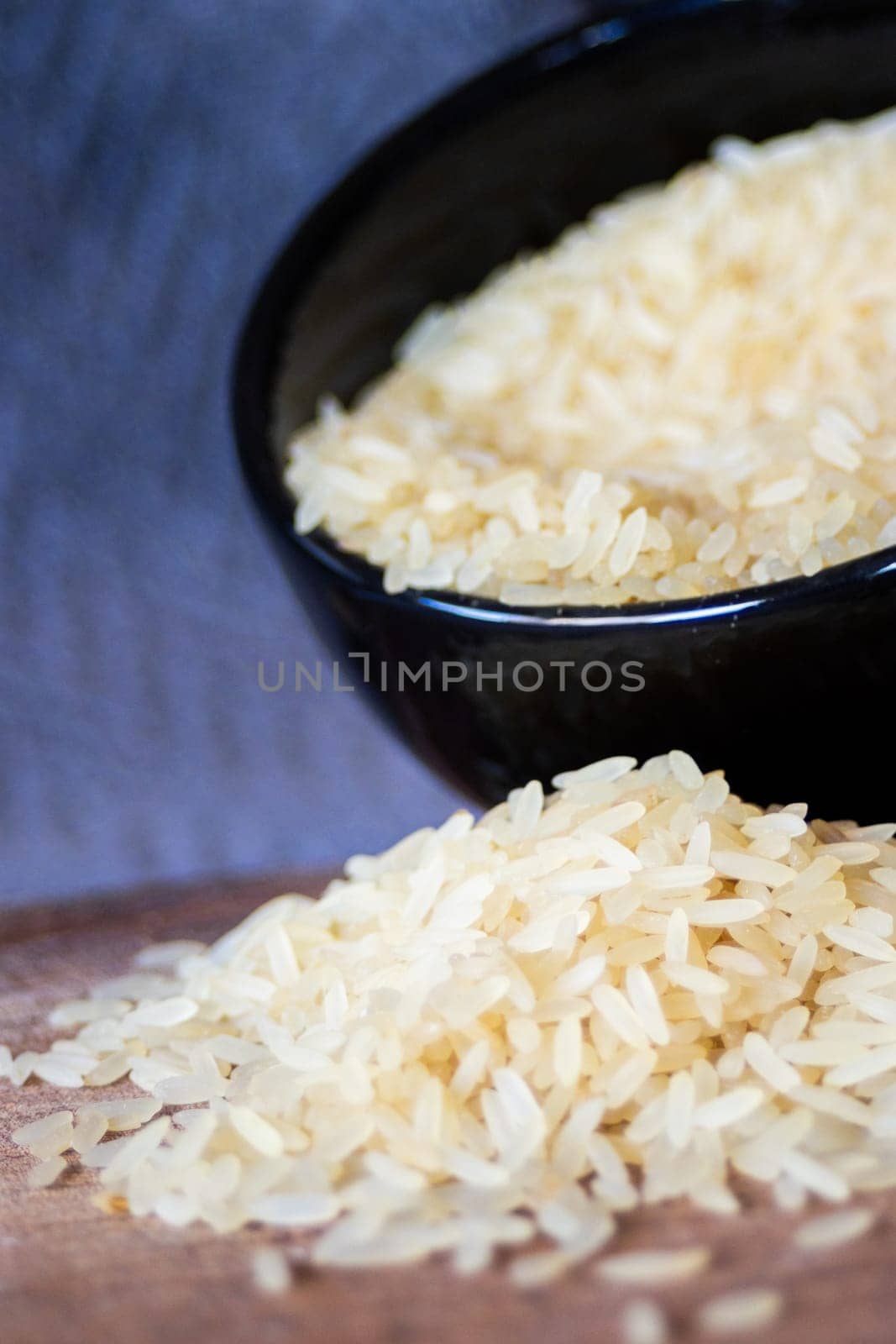 Parboiled rice grains fallin from a black bowl on wooden board.  by VeroDibe