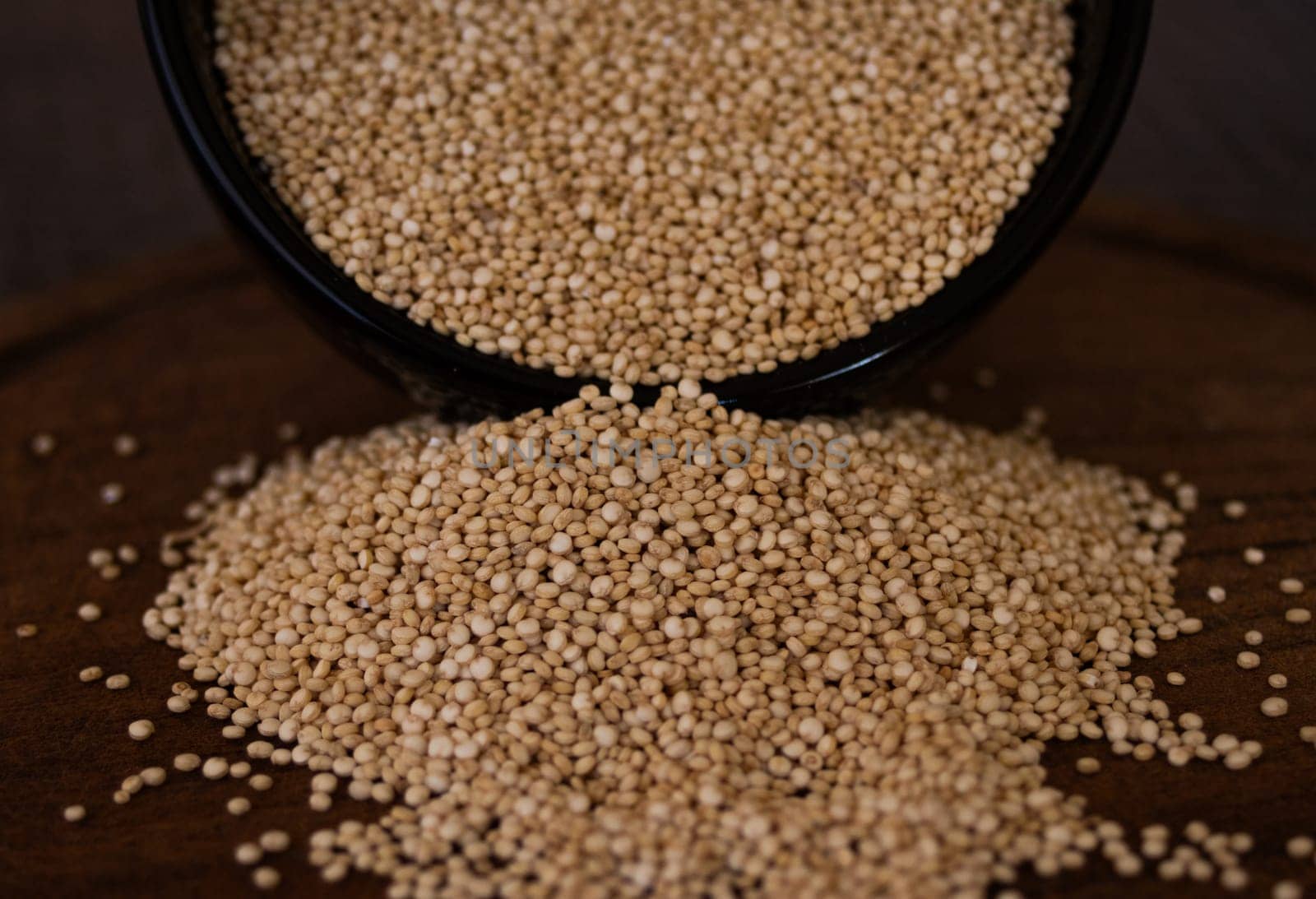 Close-up photo of quinoa grains falling on wooden board. Dark background by VeroDibe