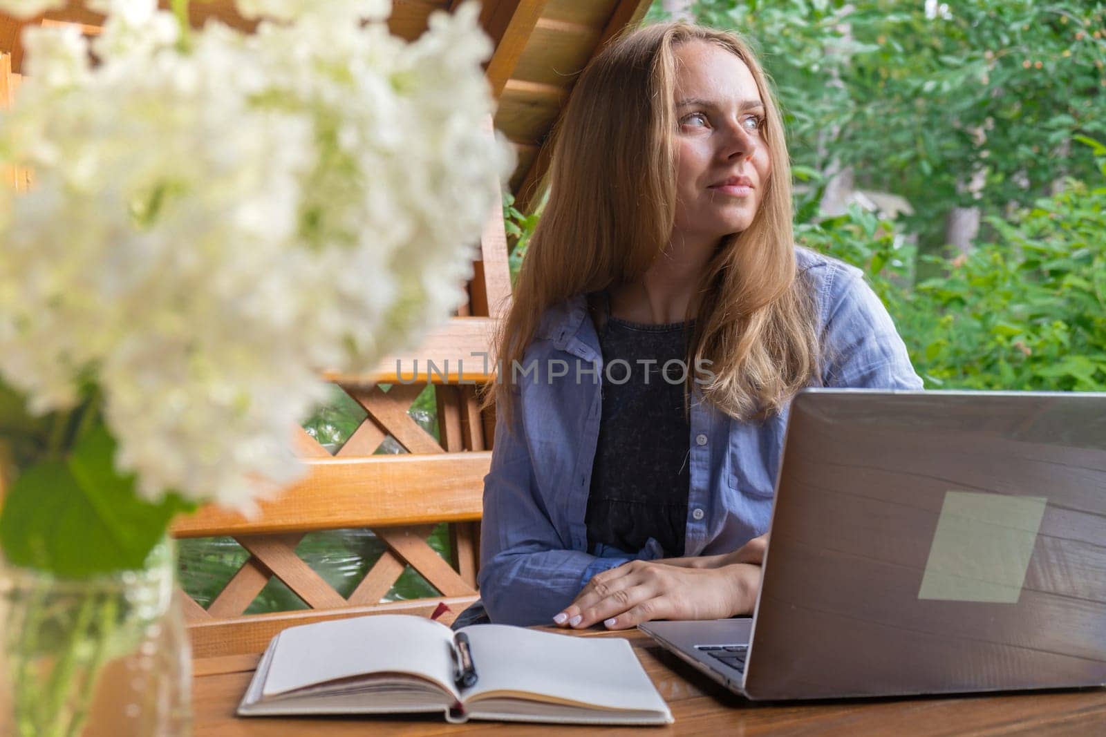 Young woman freelancer working online using laptop and enjoying the beautiful nature outdoors in garden. Online meeting education. Worcation, work from vacation, hybrid work model