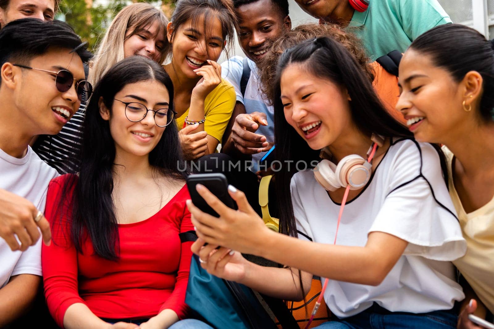 Multiracial group of teen friends looking at phone together outdoors. Social media concept.
