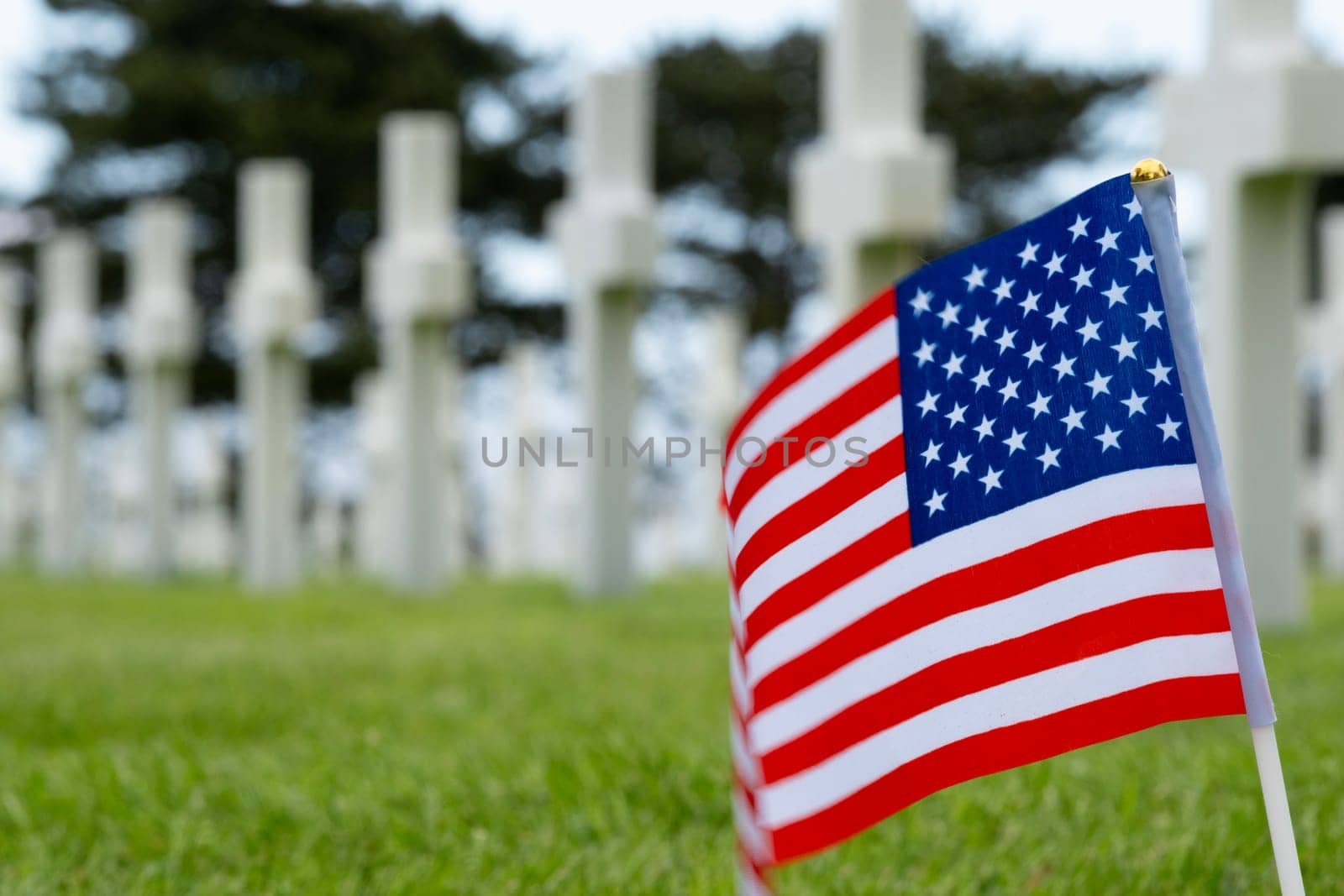 Closeup of American flag in front of American Cemetery graves at Normandy area. WWII memorial. Lines of grave stones with bright american flag. Selective focus on flag. High quality photo