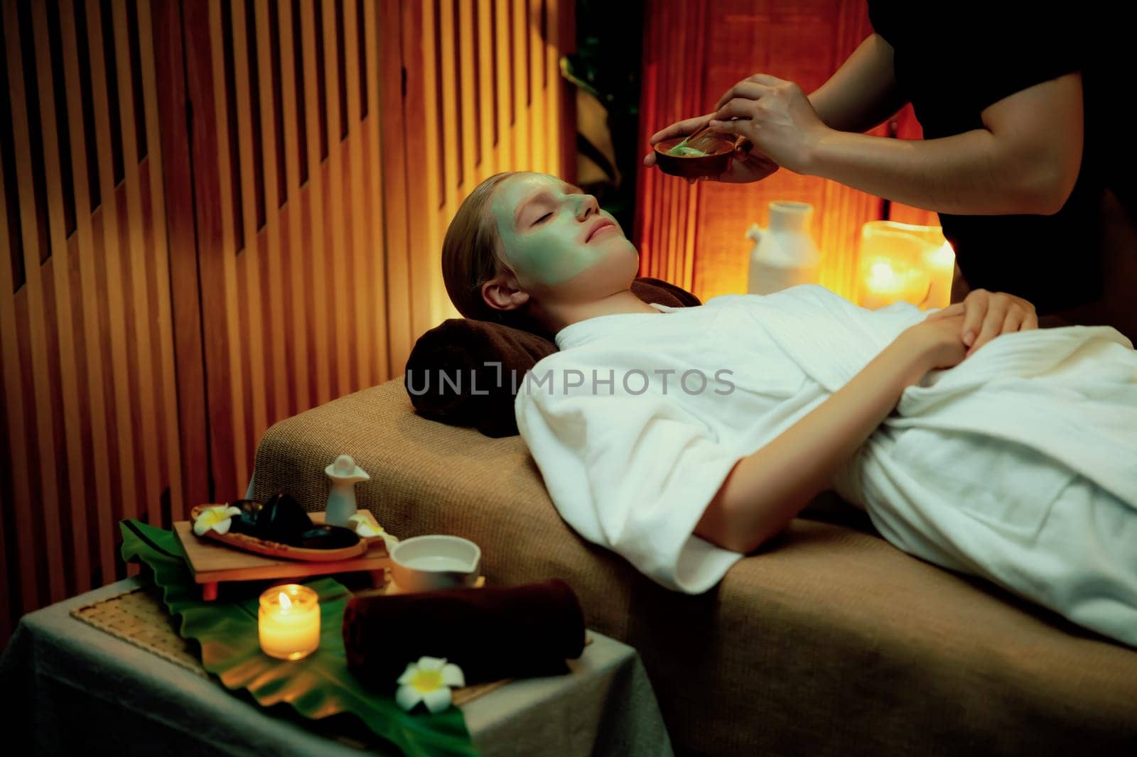 Serene ambiance of spa salon, woman customer indulges in rejuvenating with luxurious face cream massage with warm lighting candle. Facial skin treatment and beauty care concept. Quiescent