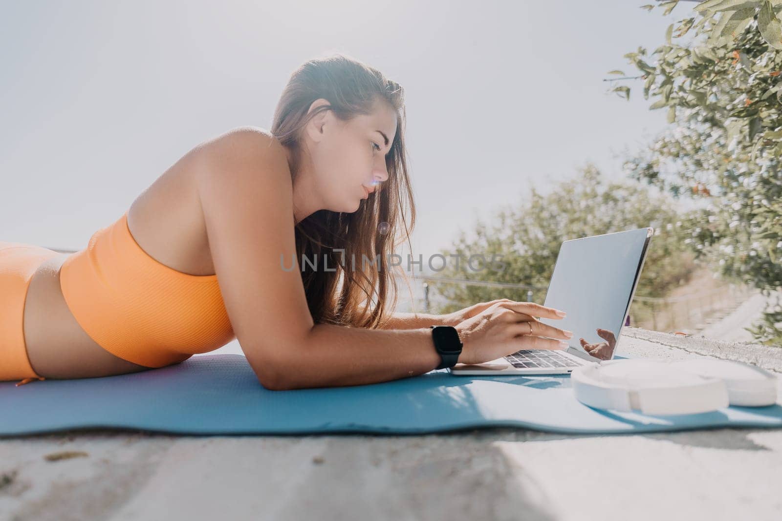 Digital nomad, Business woman working on laptop by the sea. Pretty lady typing on computer by the sea at sunset, makes a business transaction online from a distance. Freelance, remote work on vacation