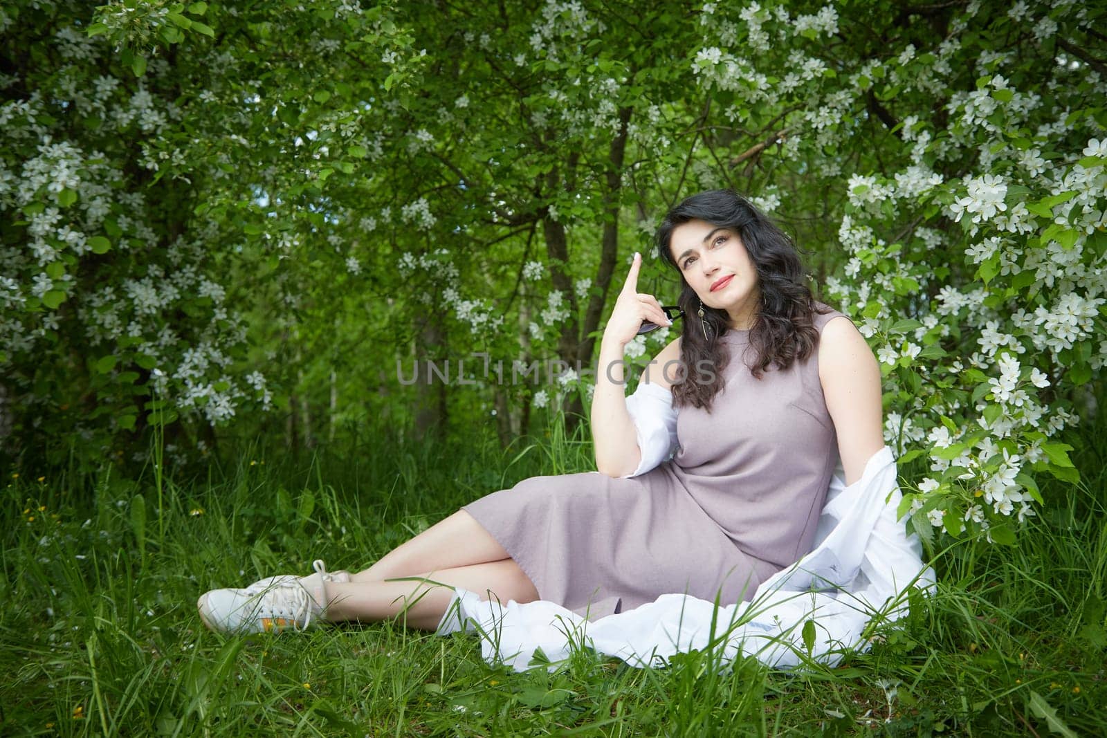Joyous brunette woman near Blossoms of apple tree in a Spring Garden outdoors. The Concept of face and body care. The scent of perfume and tenderness