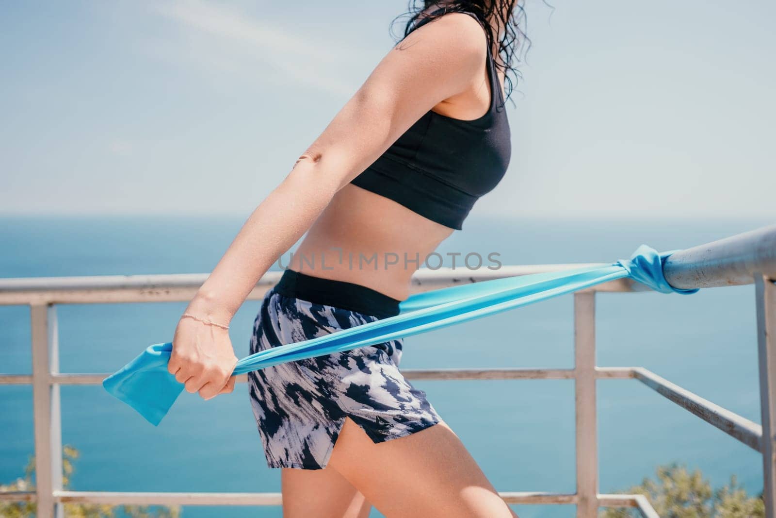 Middle aged well looking woman with black hair doing Pilates with the ring on the yoga mat near the sea on the pebble beach. Female fitness yoga concept. Healthy lifestyle, harmony and meditation.