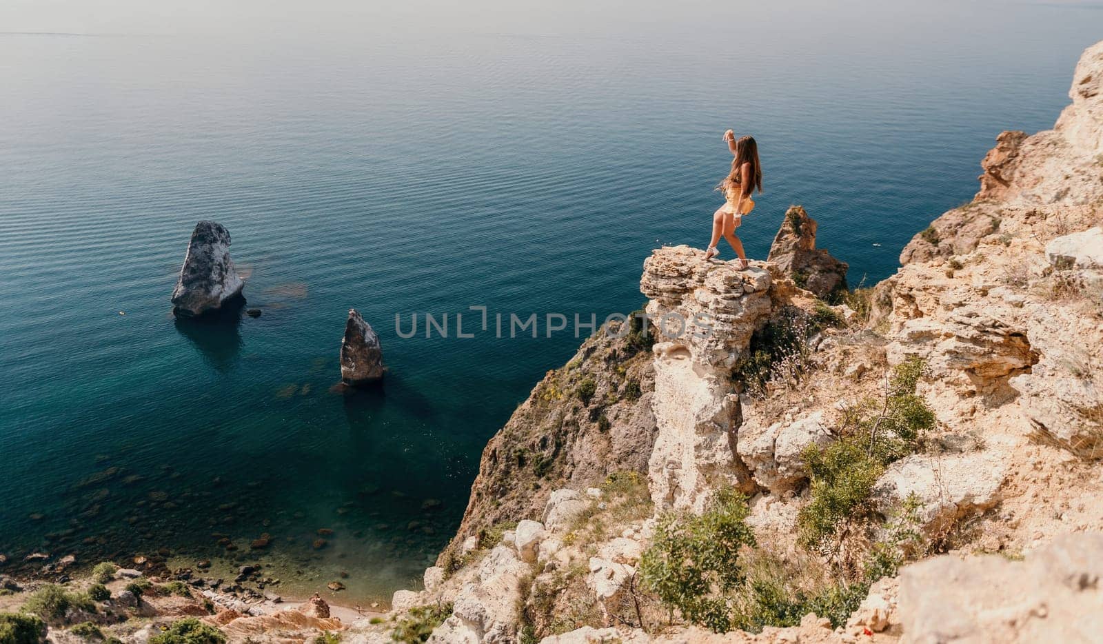 Woman travel sea. Happy tourist taking picture outdoors for memories. Woman traveler looks at the edge of the cliff on the sea bay of mountains, sharing travel adventure journey.