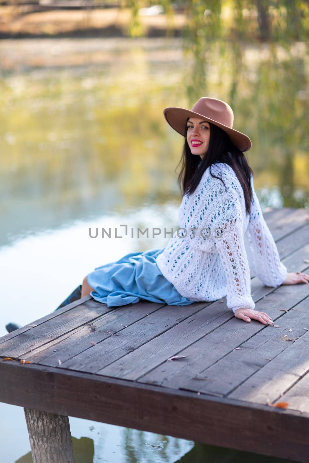 Autumn lake woman. She sits by a pond on a wooden pier in autumn and admires nature. The concept of tourism, weekends outside the city. by Matiunina