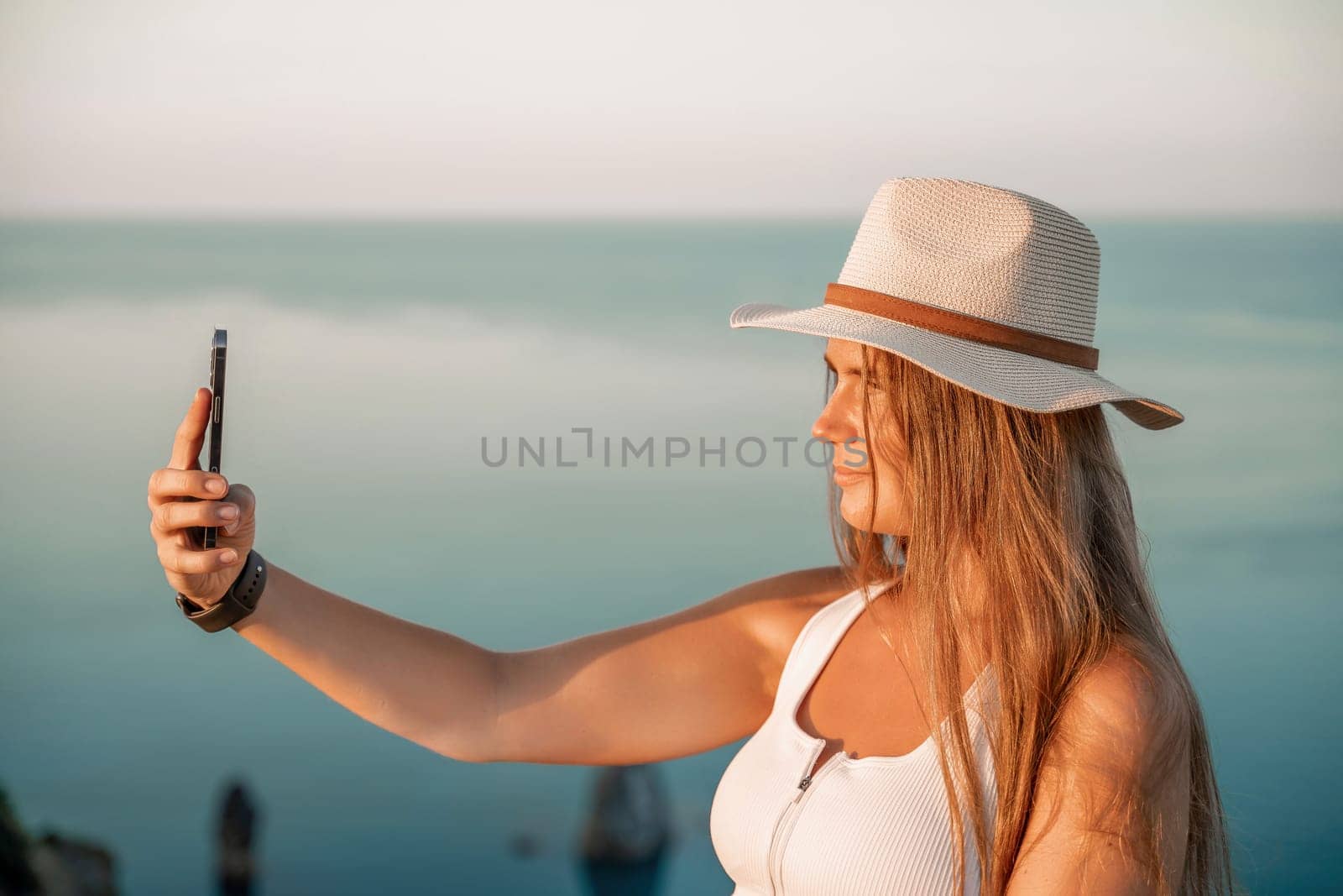 Selfie woman in hat, white tank top and shorts makes selfie shot mobile phone post photo social network outdoors on sea background beach people vacation lifestyle travel concept