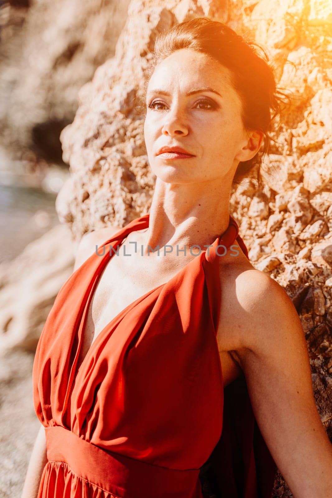 Woman red dress sea. Woman in a long red dress posing on a beach with rocks on sunny day. Girl on the nature on blue sky background