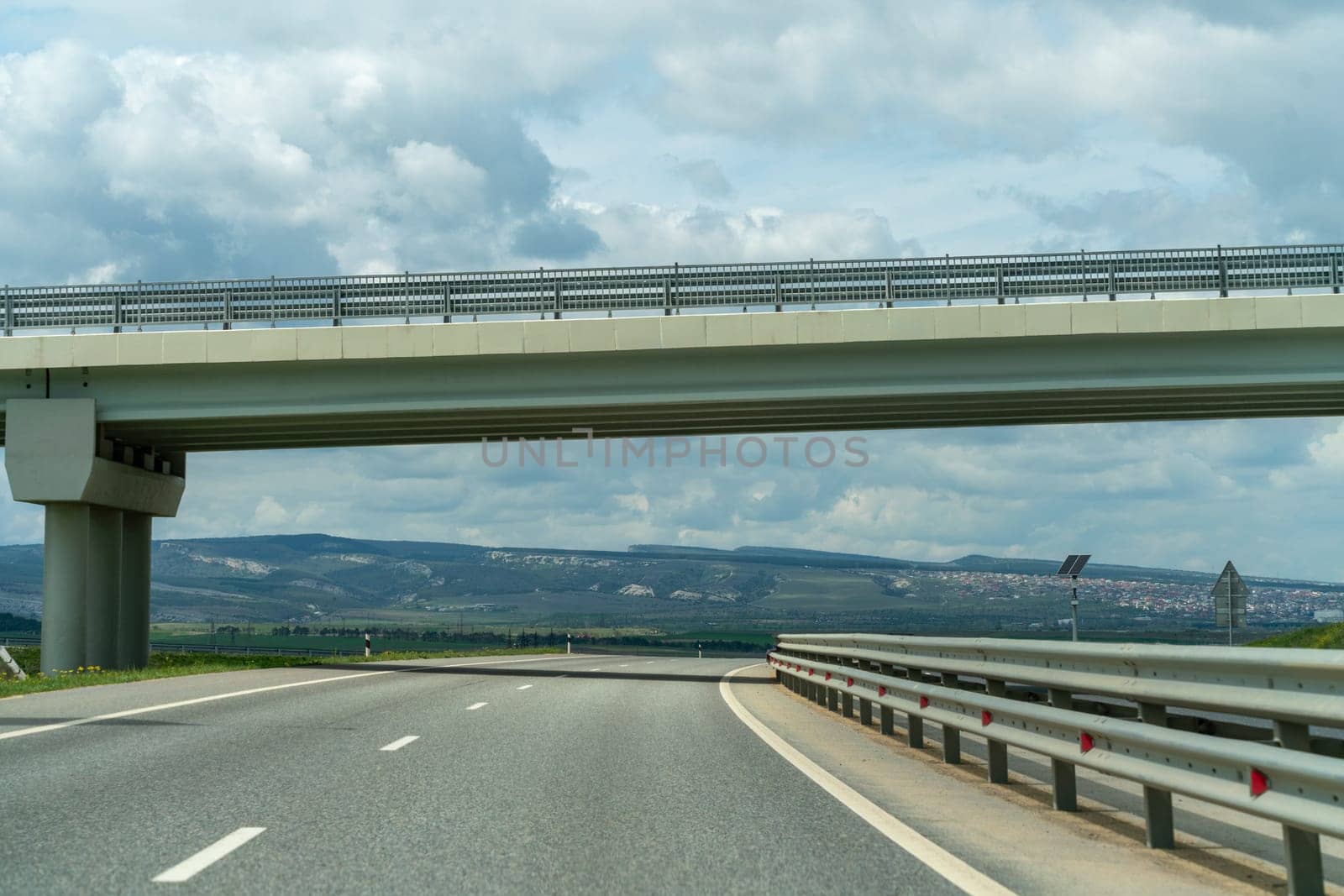 A bridge spans a road with a clear sky above. The bridge is a large structure that is visible from a distance