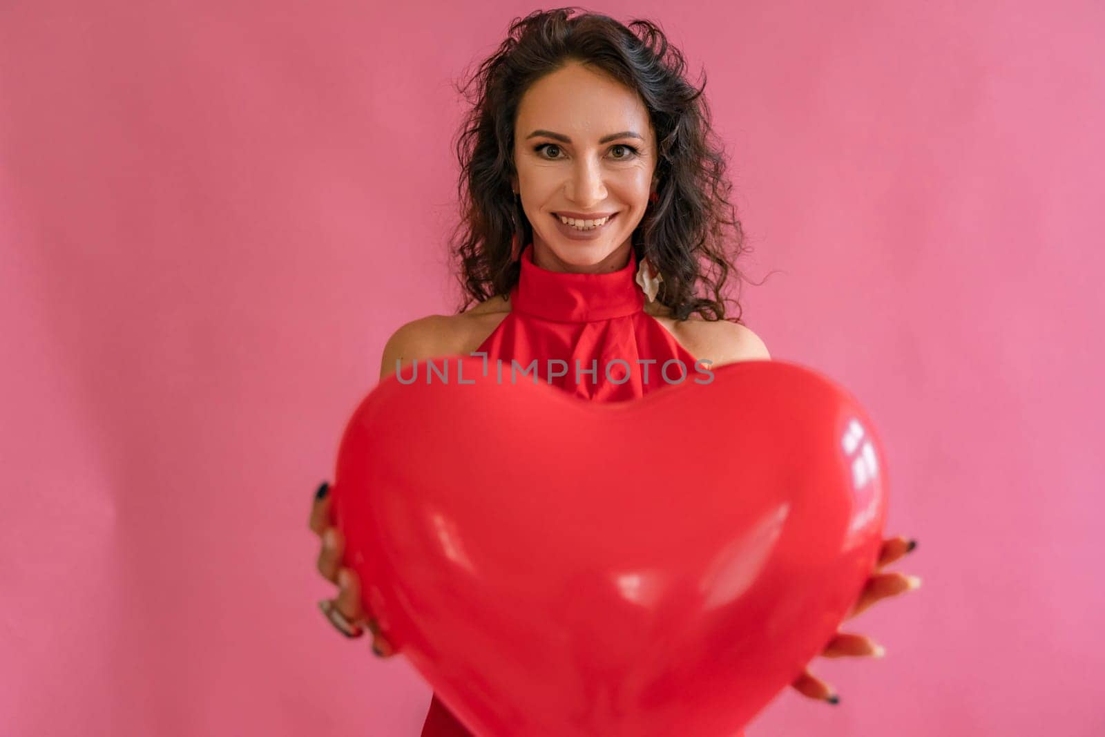 A woman is holding a red heart balloon. She is smiling and she is happy. Concept of joy and love, as the heart symbolizes affection and warmth