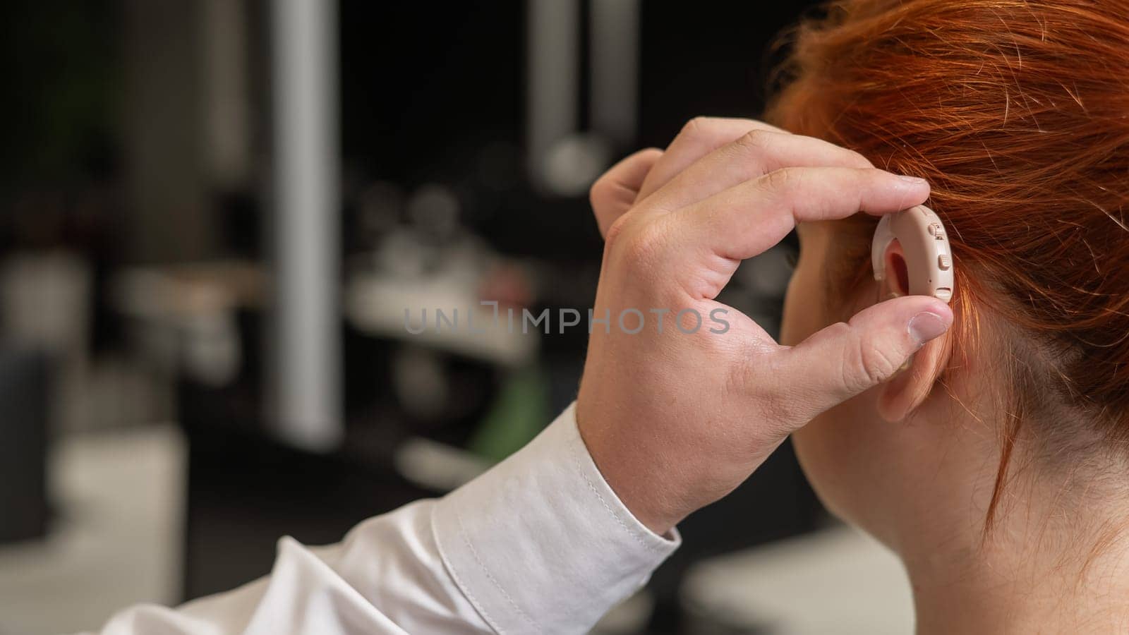 Man putting hearing aid on Caucasian red-haired woman. by mrwed54