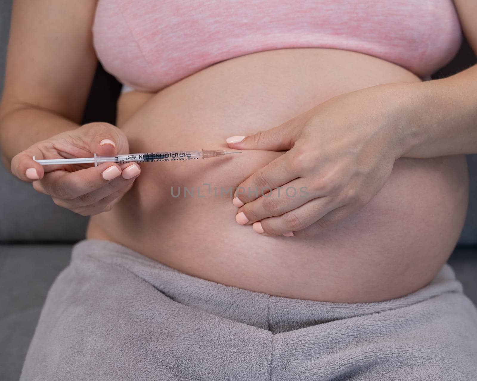 A pregnant woman puts an injection of insulin while sitting on the couch. Close up of the belly. by mrwed54
