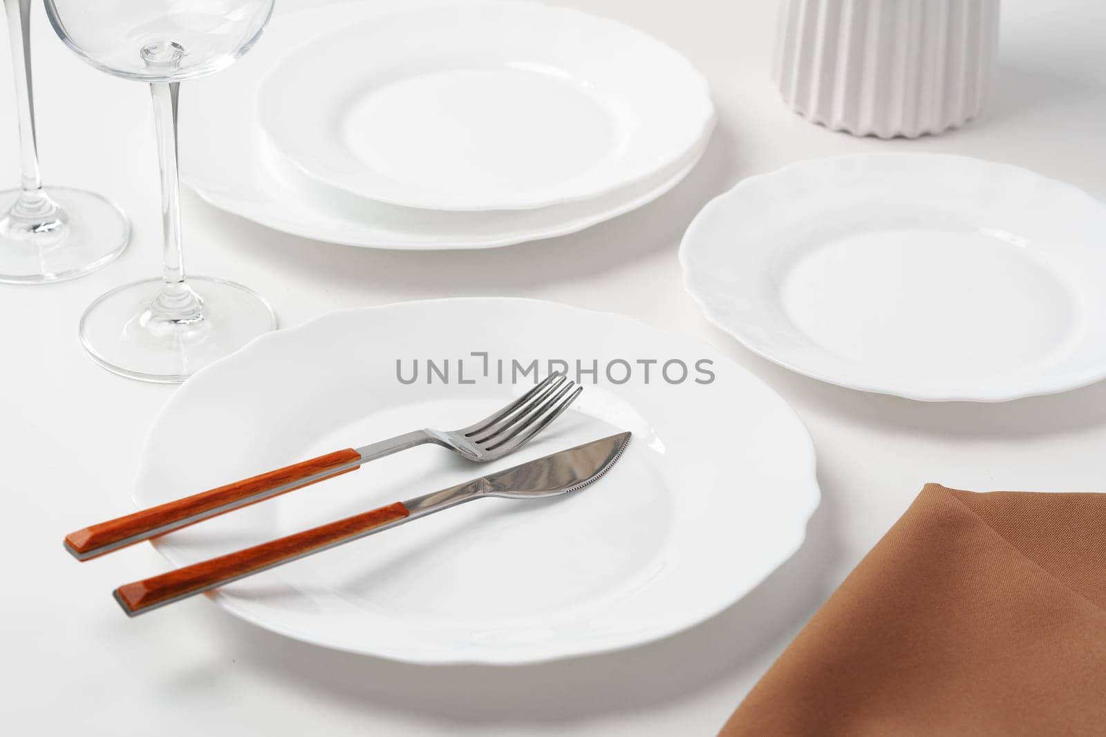 Stylish table setting with white dishware on white tablecloth close up