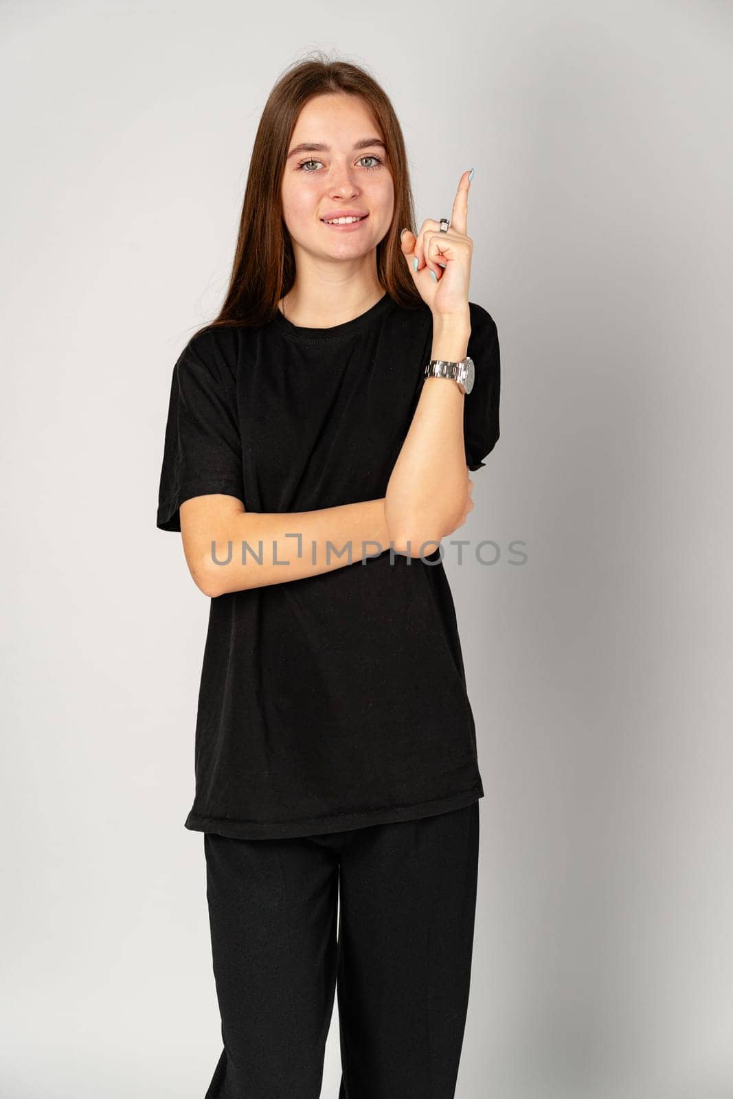 Smiling Young Woman Pointing to Copy Space Against a Grey Background in Studio