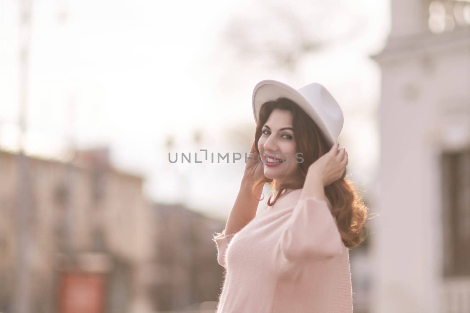 A woman wearing a white hat and a pink shirt is smiling and posing for a picture. The image has a warm and cheerful mood, with the woman's smile and the bright colors of her outfit