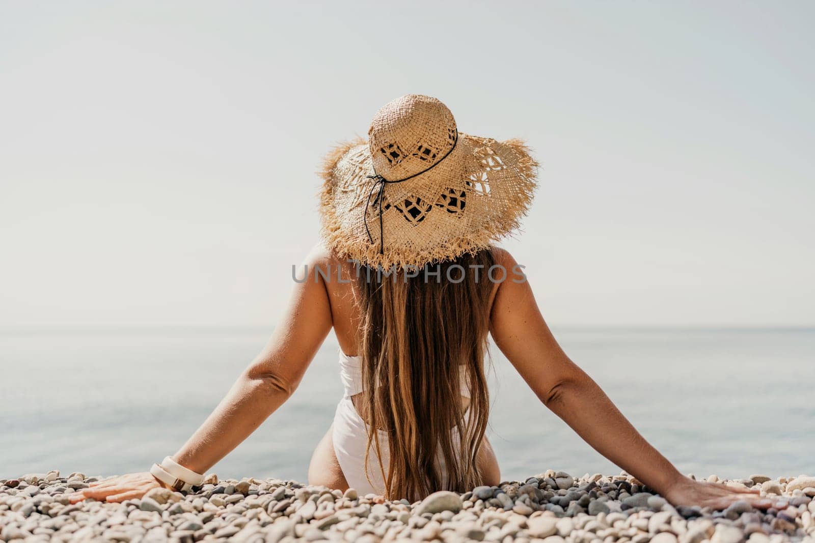 Beach Relaxation woman in hat sits on a pebble beach enjoying the sunshine. The concept of travel, vacation at sea.